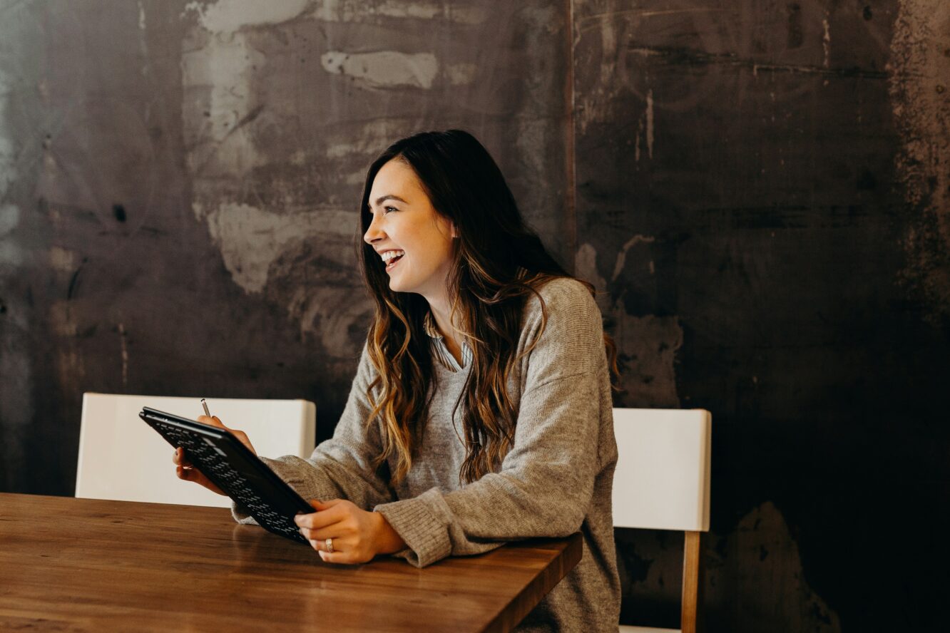 Woman holding an iPad, laughing while looking off-camera—symbolizing optimism and engagement with smart sustainability tools for small businesses.