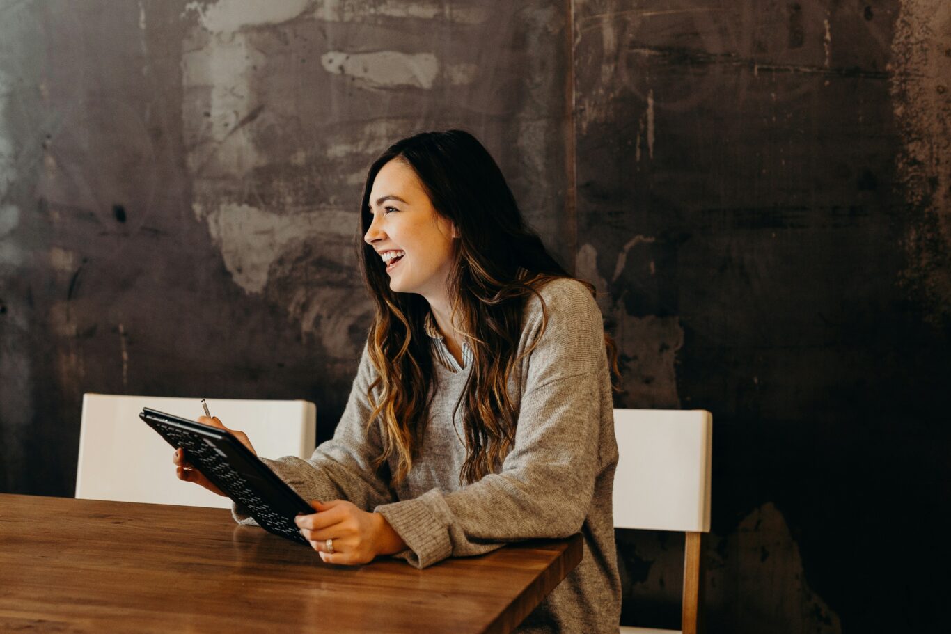 Woman holding an iPad, laughing while looking off-camera—symbolizing optimism and engagement with smart sustainability tools for small businesses.